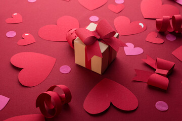 Happy st. Valentines day concept with craft paper gift box, red paper hearts, bows against dark red background with empty space for text.