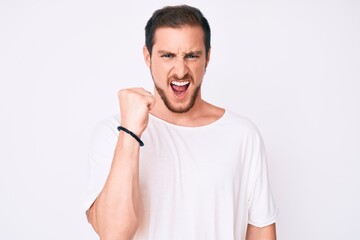 Young handsome man wearing casual white tshirt angry and mad raising fist frustrated and furious while shouting with anger. rage and aggressive concept.