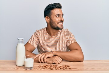 Handsome hispanic man drinking healthy almond milk looking to side, relax profile pose with natural face and confident smile.