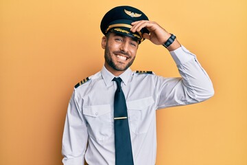 Handsome hispanic man wearing airplane pilot uniform smiling confident touching hair with hand up gesture, posing attractive and fashionable - obrazy, fototapety, plakaty