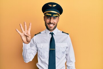 Handsome hispanic man wearing airplane pilot uniform showing and pointing up with fingers number four while smiling confident and happy. - obrazy, fototapety, plakaty