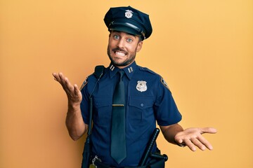 Handsome hispanic man wearing police uniform smiling cheerful with open arms as friendly welcome, positive and confident greetings