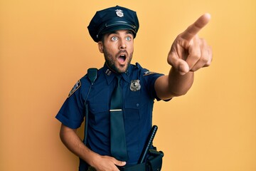 Handsome hispanic man wearing police uniform pointing with finger surprised ahead, open mouth...