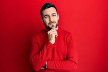 Young hispanic man wearing casual clothes smiling looking confident at the camera with crossed arms and hand on chin. thinking positive.