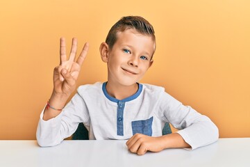 Adorable caucasian kid wearing casual clothes sitting on the table showing and pointing up with...