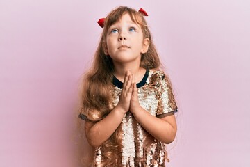Little caucasian girl kid wearing festive sequins dress begging and praying with hands together with hope expression on face very emotional and worried. begging.