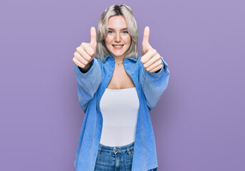Obraz na płótnie Canvas Young blonde girl wearing casual clothes approving doing positive gesture with hand, thumbs up smiling and happy for success. winner gesture.