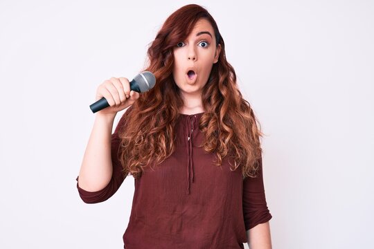 Young beautiful woman singing song using microphone scared and amazed with open mouth for surprise, disbelief face