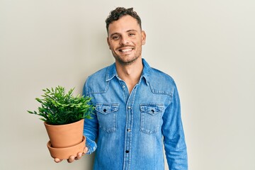 Young hispanic man holding wooden plant pot looking positive and happy standing and smiling with a confident smile showing teeth