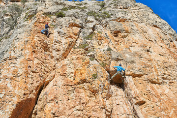 Horizontal low angle photo of two climbers climbing a reddish mountain, with blue sky on a sunny day