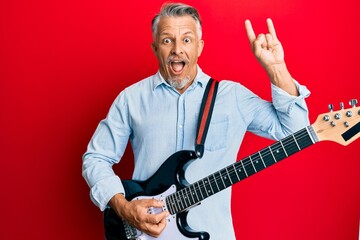 Middle age grey-haired man playing electric guitar doing rock sign celebrating crazy and amazed for...