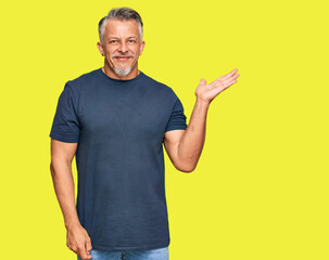 Middle age grey-haired man wearing casual clothes smiling cheerful presenting and pointing with palm of hand looking at the camera.