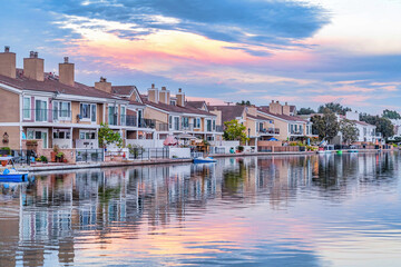 Fototapeta premium Homes in Huntington Beach with view of water reflecting cloudy sky at sunset
