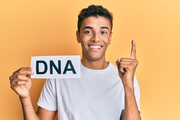 Young handsome african american man holding dna word smiling with an idea or question pointing finger with happy face, number one