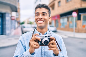 Young latin tourist man smiling happy using vintage camera walking at the city.