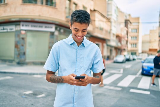 Young latin man smiling happy using smartphone walking at the city.