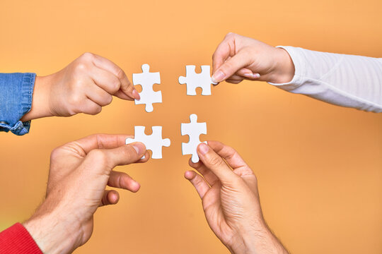 Hands of caucasian young people connecting pieces of puzzle over isolated yellow background