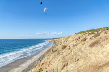 Fototapeta na wymiar Parachuters over San Diego California landscape of blue ocean and rocky mountain