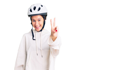 Beautiful brunette young woman wearing bike helmet and sporty clothes showing and pointing up with fingers number two while smiling confident and happy.