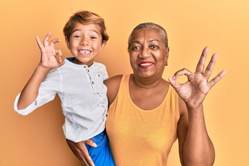 Hispanic grandson and grandmother together over yellow background doing ok sign with fingers,...
