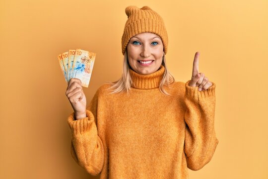 Middle age caucasian woman holding swiss franc banknotes smiling with an idea or question pointing finger with happy face, number one