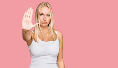 Young blonde girl wearing casual style with sleeveless shirt doing stop sing with palm of the hand....