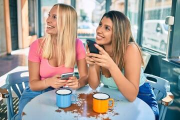 Two beautiful and young girl friends together at cafeteria using smartphone