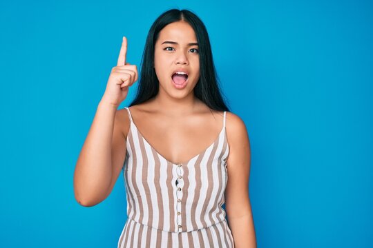 Young beautiful asian girl wearing casual clothes pointing finger up with successful idea. exited and happy. number one.