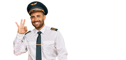 Handsome man with beard wearing airplane pilot uniform smiling positive doing ok sign with hand and fingers. successful expression.
