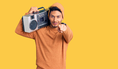 Handsome latin american young man holding boombox, listening to music pointing to you and the camera with fingers, smiling positive and cheerful