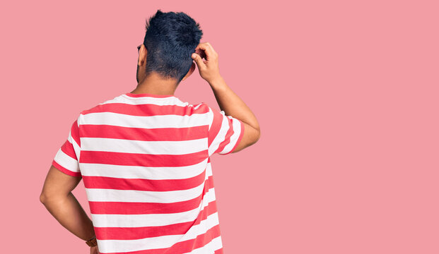 Handsome latin american young man wearing casual clothes and glasses backwards thinking about doubt with hand on head