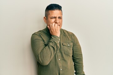 Fototapeta premium Young latin man wearing casual clothes looking stressed and nervous with hands on mouth biting nails. anxiety problem.