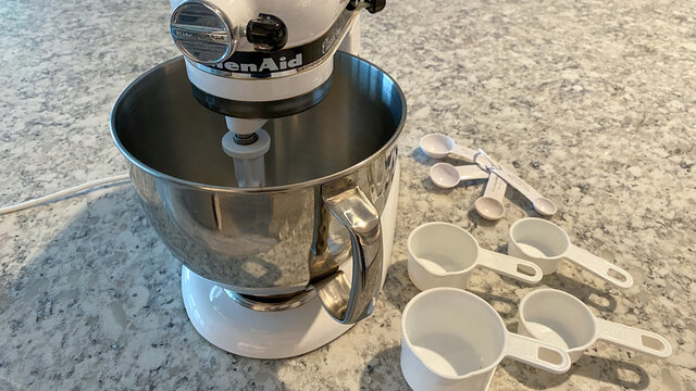 A Kitchenaid Mixer On A Kitchen Counter With Measuring Cups And Spoons Sitting Next To It.