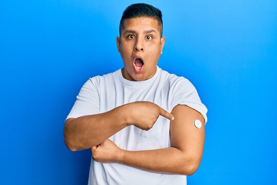 Young latin man using glucose meter button on arm afraid and shocked with surprise and amazed expression, fear and excited face.