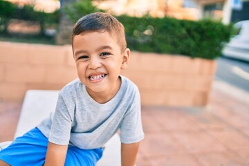 Adorable hispanic boy smiling happy sitting on the bench at the park.