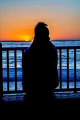 Woman silhouetted against ocean and golden sun at San Diego California sunset