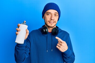 Hispanic young man wearing sweatshirt holding graffiti spray smiling happy pointing with hand and finger