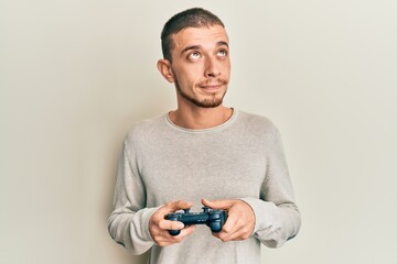 Hispanic young man playing video game holding controller smiling looking to the side and staring away thinking.