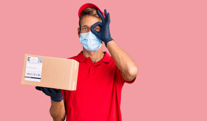 Fototapeta na wymiar Handsome blond man with beard holding delivery box wearing medical mask smiling happy doing ok sign with hand on eye looking through fingers