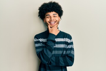 Fototapeta na wymiar Young african american man with afro hair wearing casual clothes looking confident at the camera smiling with crossed arms and hand raised on chin. thinking positive.