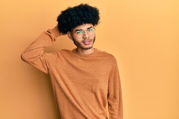 Young african american man with afro hair wearing casual winter sweater confuse and wonder about question. uncertain with doubt, thinking with hand on head. pensive concept.