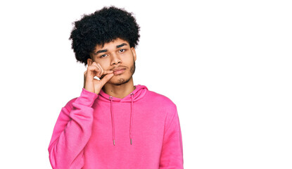 Young african american man with afro hair wearing casual pink sweatshirt mouth and lips shut as zip...