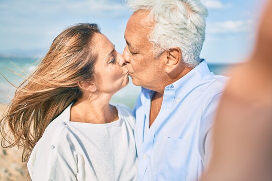 Middle age hispanic couple making selfie by the camera kissing at the beach.