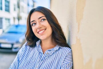 Young hispanic businesswoman smiling happy leaning on the wall at the city