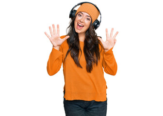 Beautiful brunette young woman listening to music using headphones showing and pointing up with fingers number nine while smiling confident and happy.