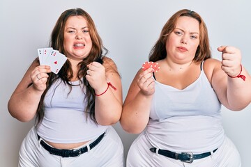 Plus size caucasian sisters woman holding poker chips and cards annoyed and frustrated shouting with anger, yelling crazy with anger and hand raised