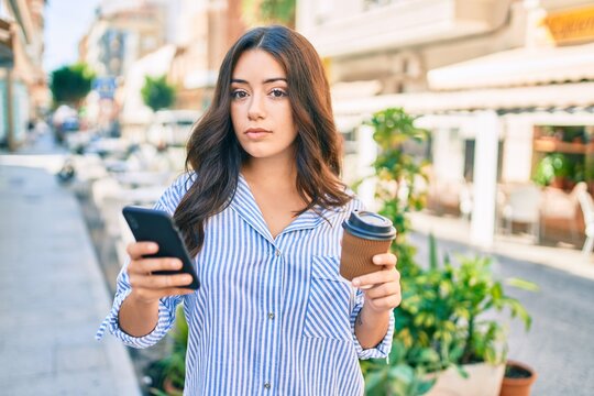 Young hispanic businesswoman using smartphone and drinking take away coffee at the city.