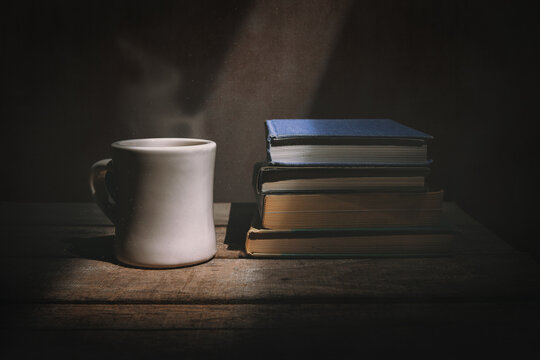 Steaming cup of coffee with a stack of books illuminated by a shaft of light