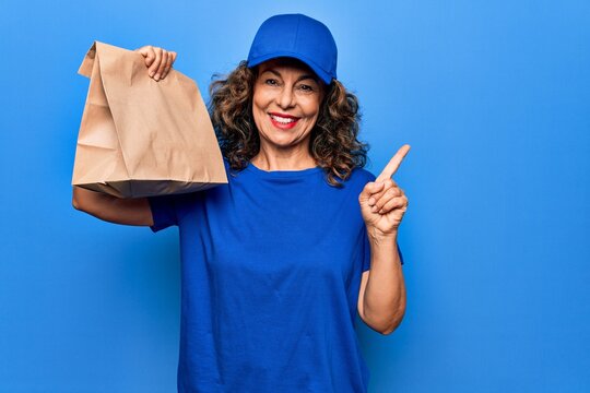 Middle age beautiful delivery woman holding deliver paper bag with takeaway food smiling happy pointing with hand and finger to the side