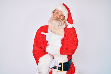 Old senior man with grey hair and long beard wearing santa claus costume with suspenders cheerful with a smile of face pointing with hand and finger up to the side with happy and natural expression